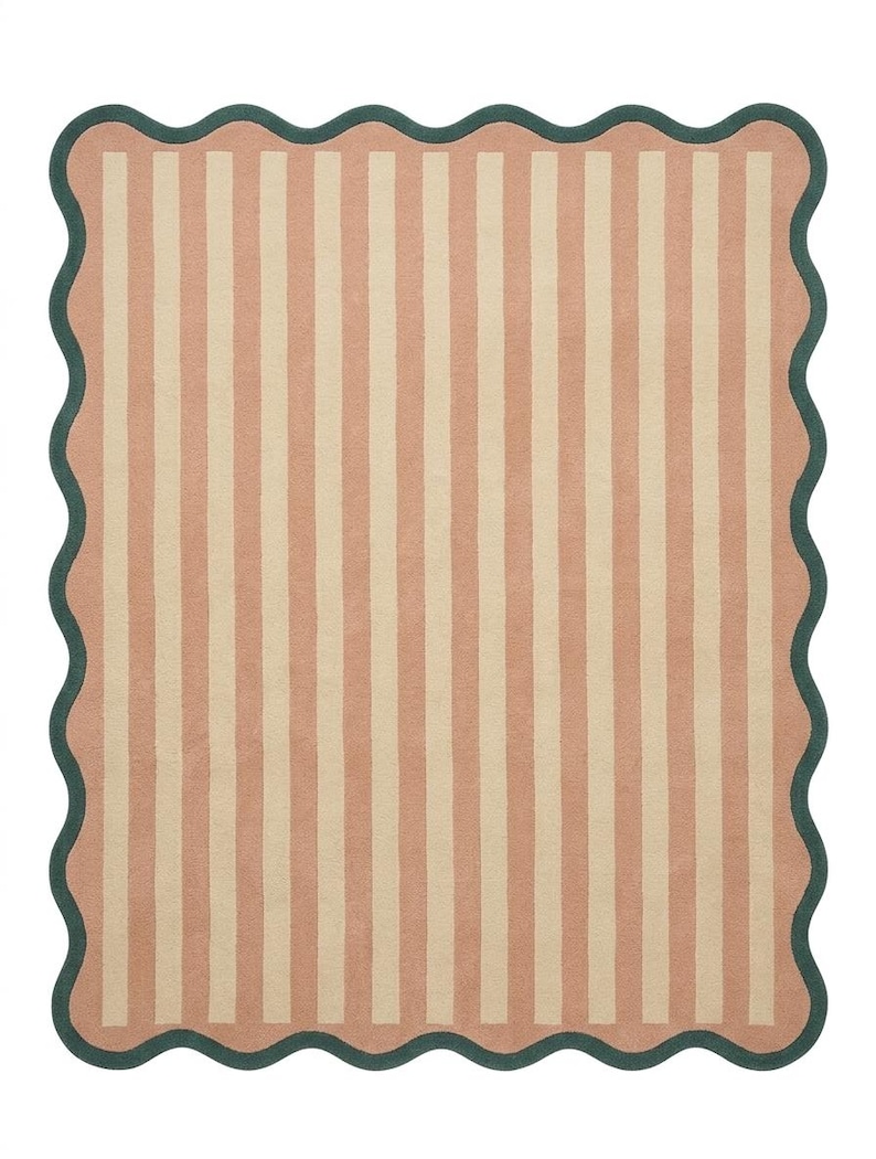 May include: A rectangular area rug featuring a pattern of vertical stripes in alternating shades of muted peach and cream. The rug is finished with a dark forest green scalloped border that follows the wavy edge of the entire piece.