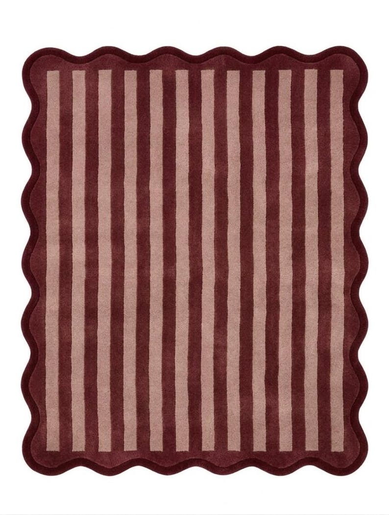 May include: A rectangular rug featuring a pattern of alternating vertical stripes in deep burgundy and soft dusty pink. The rug is finished with a continuous scalloped edge border in the same deep burgundy color, creating a wavy perimeter.