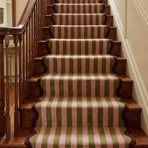 May include: A wooden staircase featuring a carpet runner with a vertical striped pattern in muted pink and olive green. The runner has a scalloped edge finished with a dark burgundy trim, extending down the center of the polished brown wooden steps.