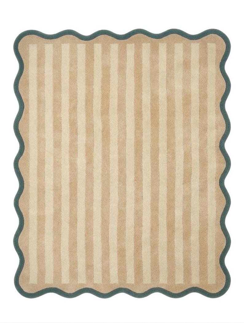 May include: A rectangular rug featuring a pattern of vertical stripes in alternating shades of tan and cream. The rug is finished with a dark teal scalloped border that follows the wavy edge of the entire perimeter of the textile piece.