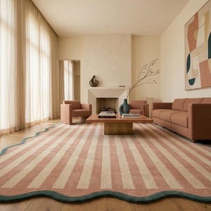 May include: A large area rug featuring vertical stripes in muted terracotta and cream colors, finished with a scalloped edge in a dark teal border. The rug is positioned on a light wood floor in a room with a sofa, armchairs, and a coffee table.