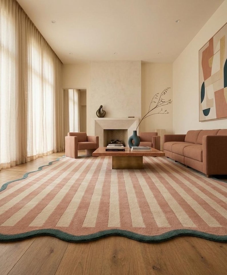 May include: A large area rug featuring vertical stripes in muted terracotta and cream colors, finished with a scalloped edge in a dark teal border. The rug is positioned on a light wood floor in a room with a sofa, armchairs, and a coffee table.