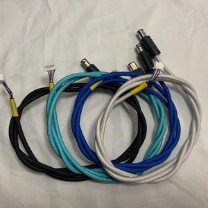May include: A selection of braided cables in black, teal, blue, and white. Each cable has connectors at one end and a bundle of wires at the other, with yellow tape details.