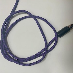 May include: A purple and black patterned cable with a black connector. The cable is coiled on a white surface. The cable is designed for electronic devices.