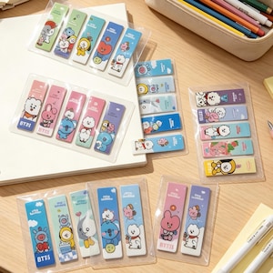 Op de afbeelding: Een verzameling rechthoekige memoblaadjes met BT21-karakterillustraties in diverse kleuren, waaronder blauw, roze, paars en groen. Elke set zit in een doorzichtige plastic verpakking en toont stripfiguren zoals RJ, Chimmy, Cooky, Koya, Mang, Shooky en Tata met de tekst BT21 op de individuele stroken.