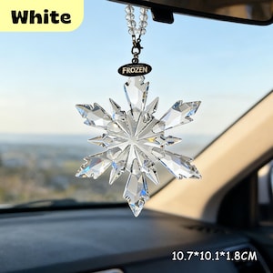 May include: A clear, crystal snowflake car charm. The charm is suspended by a beaded strand and a black tag with the word "FROZEN". The snowflake measures 10.7cm x 10.1cm x 1.8cm.