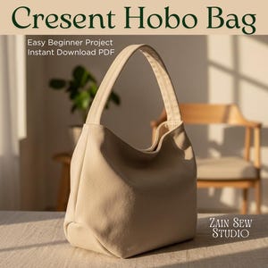 Może przedstawiać: Beżowa torba Crescent Hobo z zakrzywioną rączką. Torba wykonana jest z miękkiej, teksturowanej tkaniny i leży na neutralnej powierzchni. Tekst na zdjęciu brzmi "Cresent Hobo Bag", "Easy Beginner Project" i "Instant Download PDF". Widoczne jest również logo Zain Sew Studio.