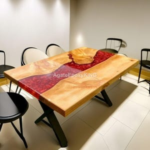 Pode incluir: Uma mesa retangular de madeira com um design de rio em resina epóxi vermelha. A mesa tem um acabamento de grão de madeira natural e pernas de metal preto. O texto "AgateEpoxyKING" é visível na superfície da mesa. A mesa é cercada por cadeiras pretas.