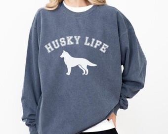 May include: A dark blue sweatshirt with the text "HUSKY LIFE" in white arched lettering above a white silhouette of a dog. The sweatshirt has a crew neck and long sleeves.