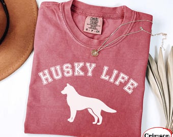 Pode incluir: Uma t-shirt de manga curta em rosa empoeirado com o texto branco HUSKY LIFE numa fonte universitária arqueada sobre uma silhueta branca de um cão husky. A etiqueta da marca Comfort Colors indica o tamanho S P CH.