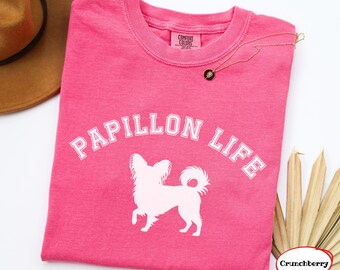 Könnte beinhalten: Ein leuchtend rosa T-Shirt mit kurzen Ärmeln, das den weißen Schriftzug PAPILLON LIFE in einer gebogenen Schriftart über einer weißen Silhouette eines Papillon-Hundes zeigt. Das Shirt hat ein Comfort Colors Etikett am Halsausschnitt.