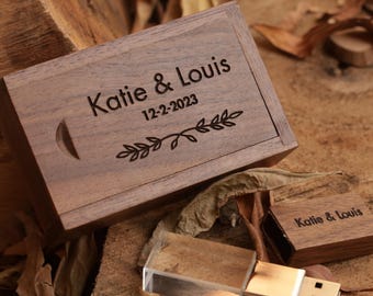 May include: A wooden USB flash drive and matching box with the names "Katie & Louis" and the date "12-2-2023" engraved on the lid. The box has a crescent moon cutout and a decorative floral design. The USB drive is silver and clear.