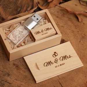Puede incluir: Una memoria USB de madera y una pequeña caja de madera con las palabras "Mr. & Mrs." grabadas. La caja está llena de virutas de madera. La tapa está abierta, revelando la memoria USB y un pequeño bloque de madera. La fecha 12.2.2023 también está grabada.