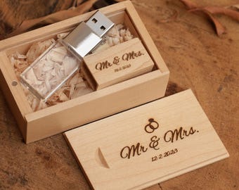 May include: A wooden USB drive and a small wooden box with the words "Mr. & Mrs." engraved on them. The box is filled with wood shavings. The lid of the box is open, revealing the USB drive and a small wooden block. The date 12.2.2023 is also engraved.