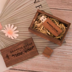 Könnte beinhalten: Holz-USB-Stick und passende Box mit dem eingravierten Namen "BRANDIE PAYNE". Der USB-Stick befindet sich in einer kleinen Holzbox, die mit Stroh gefüllt ist. Der Deckel der Box und ein kleines Holzquadrat sind ebenfalls sichtbar. Das Datum 13-4-2023 ist ebenfalls graviert.
