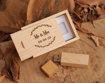 Könnte beinhalten: Ein USB-Stick aus Holz und eine passende Box mit Schiebedeckel. Die Box ist mit "Mr & Mrs" und dem Datum "04-04-23" in einem dekorativen Kranz graviert. Der USB-Stick und die Box sind aus hellem Holz.