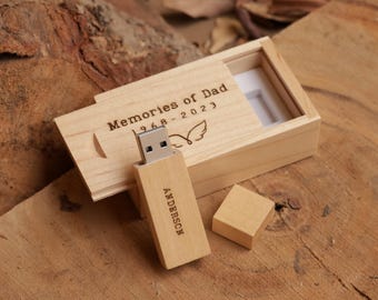 May include: A wooden USB flash drive and matching box. The flash drive is engraved with the name "Anderson". The box lid reads "Memories of Dad 1968-2023" with a wing graphic. The items are on a wooden surface.