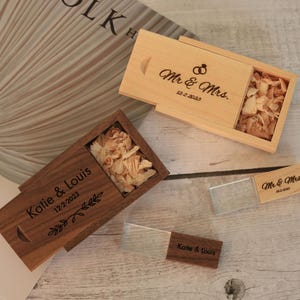 Könnte beinhalten: Zwei USB-Sticks aus Holz und zwei Holzkisten mit Schiebedeckeln. Eine Kiste ist hellfarbig mit "Mr. & Mrs." und dem Datum 12-2-2023. Die andere Kiste ist dunkel gefärbt mit "Katie & Louis" und dem Datum 12-2-2023.