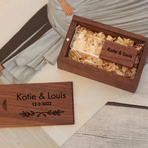 Peut inclure: Ensemble de clé USB et boîte en bois. La boîte est remplie de copeaux de bois et comprend une petite étiquette en bois. La clé USB et l'étiquette sont gravées des noms "Katie & Louis" et de la date "12-2-2023", ainsi qu'un croissant de lune et un motif de feuilles.