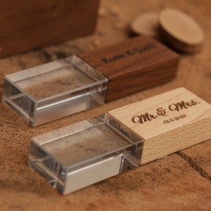 May include: Two wooden USB flash drives with clear plastic covers. One is engraved with "Kathy & David", the other with "Mr. & Mrs." and a date. The wood has a natural grain, and the background is a wooden surface.