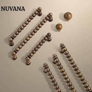 May include: A collection of bronze-coloured cabinet pulls and knobs. The pulls are long and feature a series of small, round beads. The knobs are spherical. The word "NUVANA" is printed in the upper left corner.