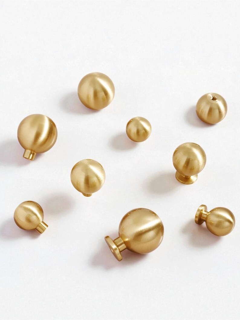 May include: A selection of brass cabinet knobs in different sizes, displayed on a white background. The knobs are spherical with a polished, gold finish. Some have a stem and base for mounting.