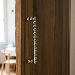 Peut inclure: Gros plan sur une porte en bois avec une poignée argentée. La poignée est composée de petites sphères argentées rondes disposées en ligne verticale. Le bois a un veinage naturel.