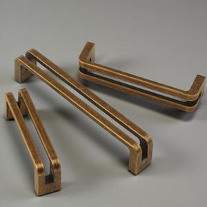 Pode incluir: Várias puxadores de armário em latão antigo em vários tamanhos. Cada puxador tem uma forma retangular com um design de barra dupla. Os puxadores são de uma cor latão envelhecido, sugerindo uma estética vintage. Adequado para gavetas e armários.