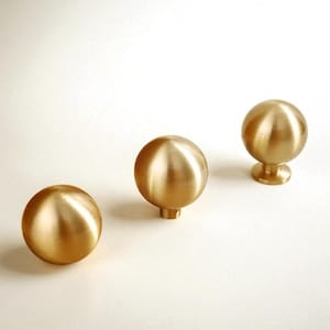 May include: Three brass cabinet knobs with a spherical design. The knobs have a polished finish and are arranged on a white surface. The knobs are approximately 3.8 cm in diameter.