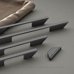 Op de afbeelding: Een set matzwarte kastgrepen en een bijpassende knop. De grepen zijn rechthoekig met een afgeschuinde rand en de knop heeft een trapeziumvorm. De hardware wordt gepresenteerd op een grijze ondergrond.