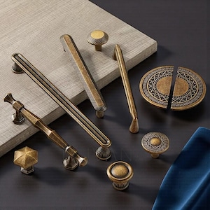 Pode incluir: Uma variedade de ferragens de armário em latão antigo, incluindo puxadores, puxadores e uma placa oval decorativa. As ferragens apresentam vários designs, como padrões geométricos e superfícies texturizadas, com um acabamento quente e envelhecido.