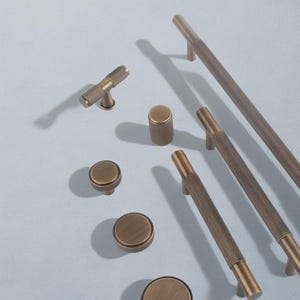 Könnte beinhalten: Eine Auswahl an antiken Messing-Schrankbeschlägen, darunter Knöpfe und Griffe. Die Beschläge weisen ein strukturiertes, rautenförmiges Design auf. Die Kollektion umfasst verschiedene Größen und Formen.