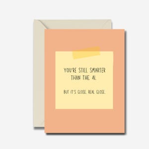 Pode incluir: Um cartão com fundo cor de pêssego e um post-it amarelo. O post-it diz: "VOCÊ AINDA É MAIS INTELIGENTE QUE A IA. MAS ESTÁ PERTO. MUITO PERTO." O cartão está dentro de um envelope creme.