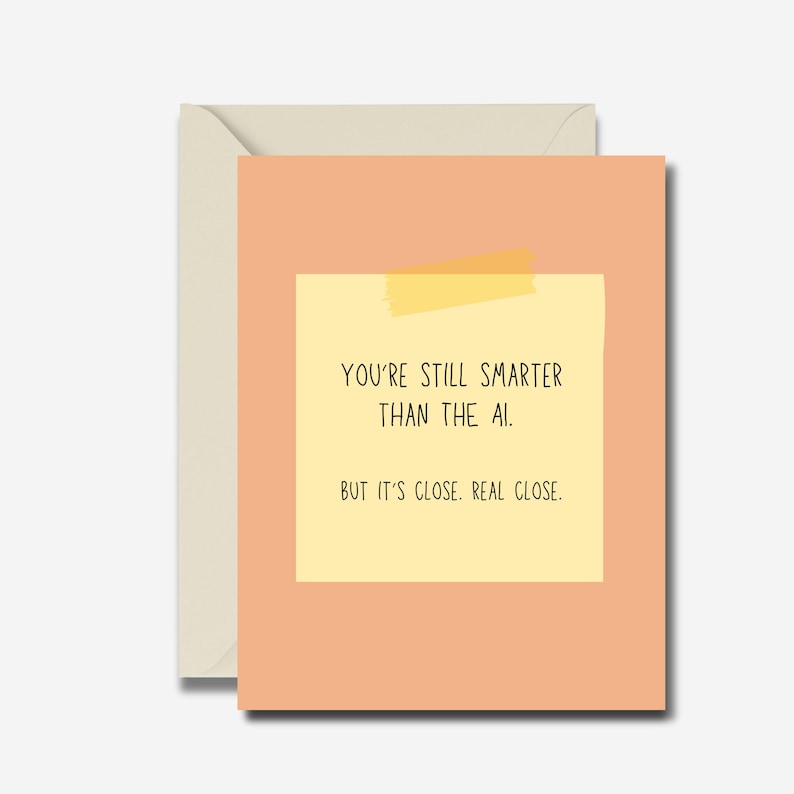 May include: A greeting card with a peach-colored background and a yellow sticky note. The note reads, "YOU'RE STILL SMARTER THAN THE AI. BUT IT'S CLOSE. REAL CLOSE." The card is inside a cream-colored envelope.