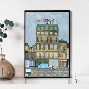 May include: A framed art print of "The French Dispatch" movie poster. The artwork depicts a European street scene with buildings, a blue van, and a person on a scooter. The poster includes the movie title and cast names.