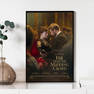 May include: A framed movie poster for "Far From The Madding Crowd" shows a couple dancing. The poster has a dark background with the movie title and cast names at the bottom. The poster is in a black frame.