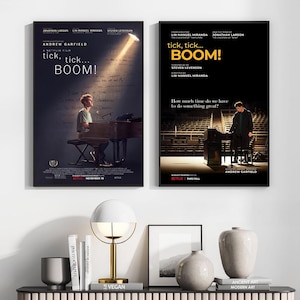 Może przedstawiać: Dwa oprawione plakaty filmowe do filmu "tick, tick... BOOM!" z Andrewem Garfieldem. Lewy plakat ma ciemne tło z tytułem i osobą przy pianinie. Prawy plakat jest czarny z tytułem i osobą przy pianinie. Lampa, książki i wazony znajdują się na półce.