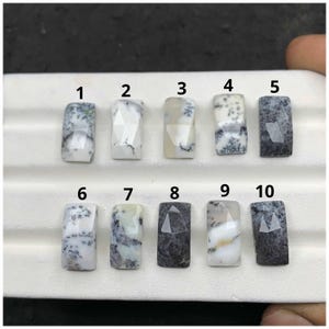 May include: Ten rectangular, faceted gemstones with varying patterns of white, grey, and black. Each stone is numbered from 1 to 10. The gemstones are displayed on a white surface, showcasing their unique textures and colours.