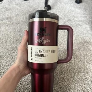 May include: A burgundy Stanley Quencher H2.0 Tumbler with a handle. The tumbler has a black lid and a white label with the text "QUENCHER H2.0 TUMBLER". The tumbler is designed for all-day hydration and holds 40 oz / 1.18L.