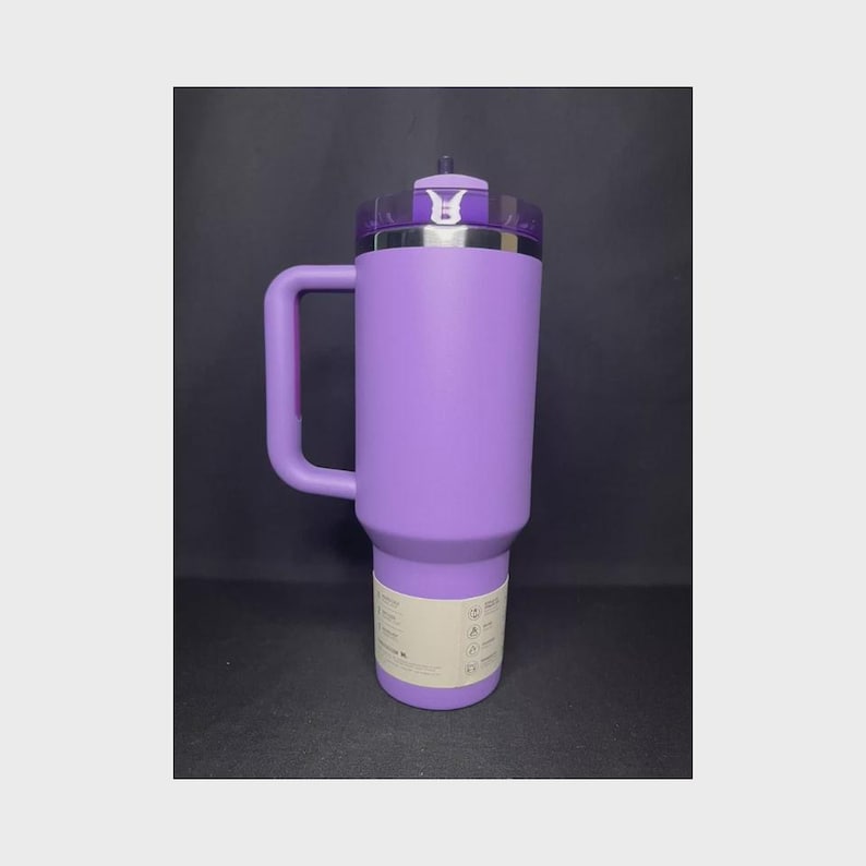 Op de afbeelding: Een grote, paarse ge&iuml;soleerde beker met een handvat. De beker heeft een doorzichtig deksel met een zilveren rand en een klein decoratief embleem. Een wit etiket met tekst is aan de onderkant van de beker bevestigd.