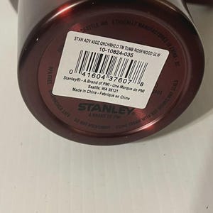 May include: A maroon Stanley brand tumbler with a white label. The label includes the text "STAN ADV 400Z QNCHRH2.0 TM TUMB ROSEWOOD GLW" and a barcode. The tumbler is BPA free and dishwasher safe.