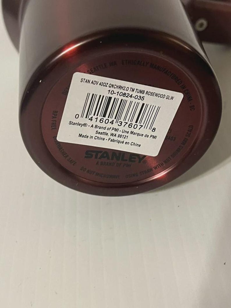 May include: A maroon Stanley brand tumbler with a white label. The label includes the text "STAN ADV 400Z QNCHRH2.0 TM TUMB ROSEWOOD GLW" and a barcode. The tumbler is BPA free and dishwasher safe.