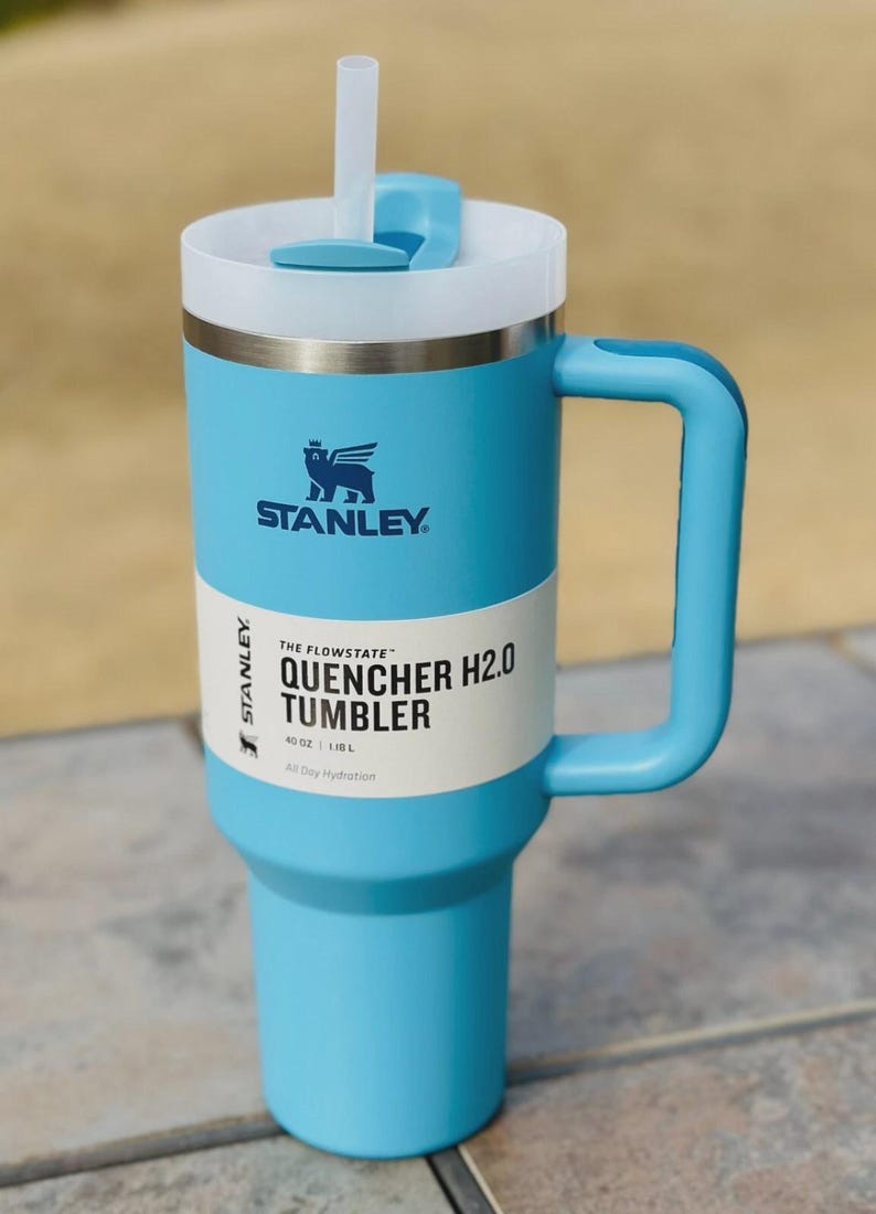 May include: A light blue Stanley Quencher H2.0 tumbler with a white lid and handle. The tumbler features the Stanley logo and text reading "Quencher H2.0 Tumbler" and "40 OZ | 1.18L". Includes a white straw.