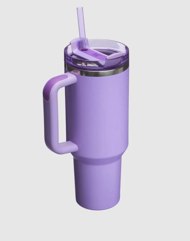Op de afbeelding: Een lavendelkleurige ge&iuml;soleerde beker met een handvat en een doorzichtig deksel. De beker heeft een bijpassend lavendelkleurig rietje en een zilveren rand. Het handvat is gebogen en aan de zijkant van de beker bevestigd.