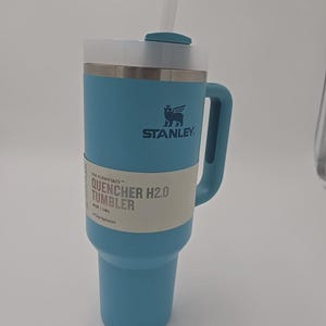 May include: A light blue Stanley Quencher H2.0 tumbler with a handle and straw. The tumbler has a white band with the text "QUENCHER H2.0 TUMBLER" and the Stanley logo. It holds 1.18L and is designed for all-day hydration.