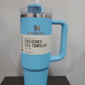 May include: A light blue Stanley Quencher H2.0 Tumbler with a handle and straw. The tumbler has a clear lid and a white label with the text "QUENCHER H2.0 TUMBLER" and "30 OZ | .88 L". The Stanley logo is visible on the front.