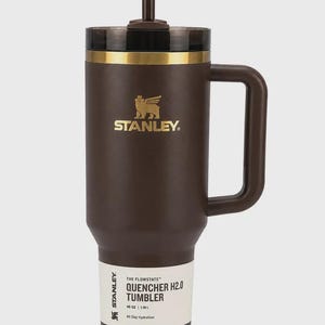 Peut inclure: Gobelet Stanley Flowstate Quencher H2.0 marron avec une poign&eacute;e et une paille. Le gobelet a un bord dor&eacute; et le logo Stanley en or. L'&eacute;tiquette indique "40 oz | 1,18 L" et "All Day Hydration".
