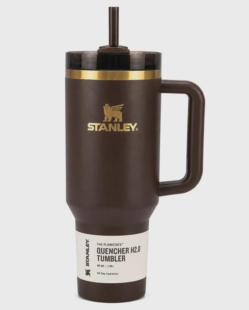 Peut inclure: Gobelet Stanley Flowstate Quencher H2.0 marron avec une poign&eacute;e et une paille. Le gobelet a un bord dor&eacute; et le logo Stanley en or. L'&eacute;tiquette indique "40 oz | 1,18 L" et "All Day Hydration".
