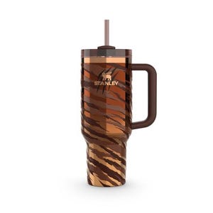 May include: A Stanley insulated tumbler with a handle and straw. The tumbler has a brown and tan tiger stripe pattern. The Stanley logo is visible on the front. Designed to keep drinks cold or hot. Holds approximately 946 ml.