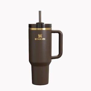 Peut inclure: Gobelet isotherme marron avec une poign&eacute;e et une paille. Le gobelet pr&eacute;sente une bande dor&eacute;e et le logo Stanley. Con&ccedil;u pour garder les boissons chaudes ou froides pendant des heures. Id&eacute;al pour les d&eacute;placements.
